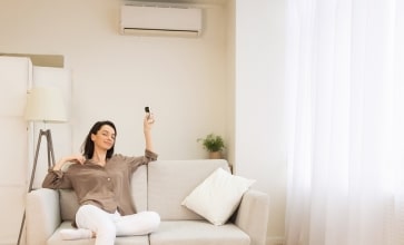 Femme actionnant la télécommande de sa climatisation réversible depuis son canapé